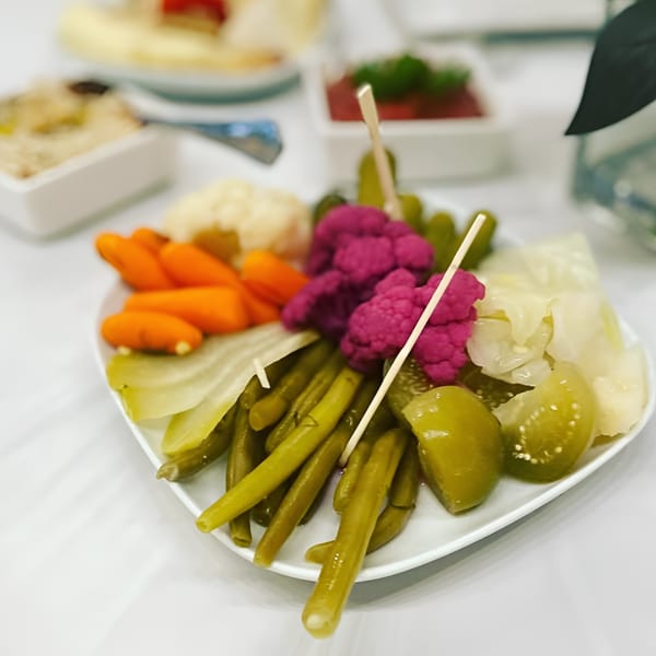 A white plate filled with an assortment of pickled vegetables, including purple cauliflower, carrots, and green beans.
