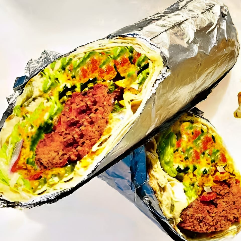 Two Asteria Restaurant Mediterranean wraps, cut in half, revealing meat, lettuce, and sauce, wrapped in foil.