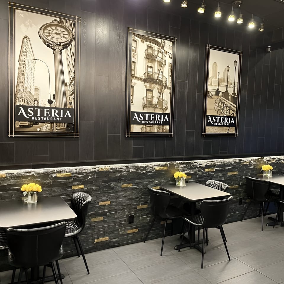 Asteria Restaurant's dining area features black tables, chairs, and wall art against a dark, textured wall.