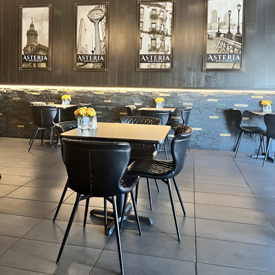Interior of Asteria Restaurant with black tables and chairs, and cityscape art on dark wood walls.