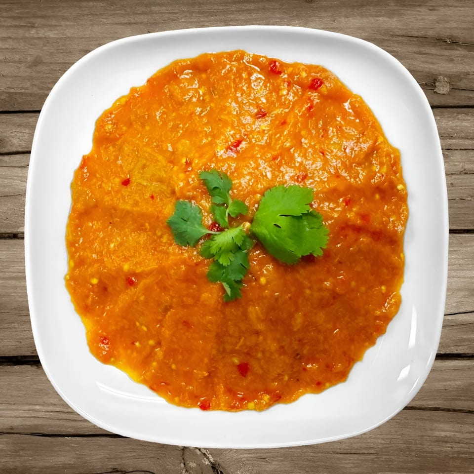 A Mediterranean dip, orange with red flecks, garnished with cilantro on a white plate.